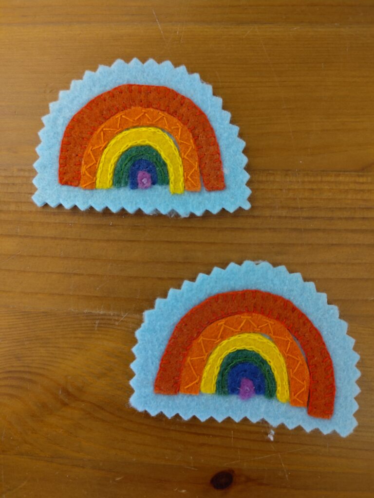 Zwei Regenbogen-Patches aus Filz, von Hand bestickt.